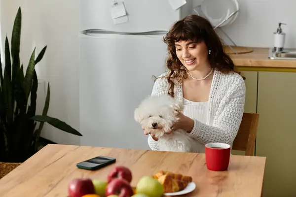 A young woman smiles with her fluffy puppy at a rustic table filled with breakfast items. — Stock Photo