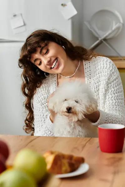 A smile lights up a young womans face as she cuddles her fluffy dog while enjoying breakfast — Stock Photo