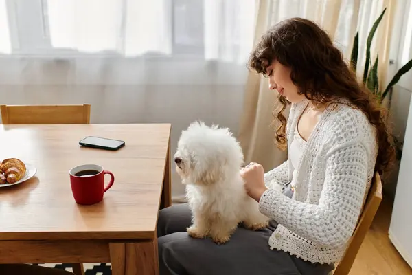 Sipping coffee, a young woman enjoys a cozy moment with her fluffy dog at home. — Stock Photo