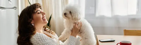 A young woman happily interacts with her fluffy white dog in a bright kitchen filled with light. — Stock Photo
