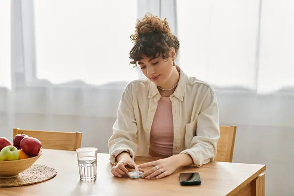 A young woman relaxes at a wooden table in her home, absorbed in her phone amidst apples and water. — Stock Photo
