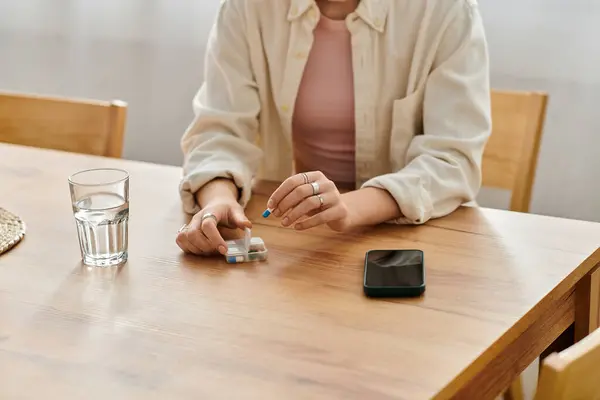 A young woman sits at a wooden table, reflecting while holding medication and a phone nearby. — Stock Photo
