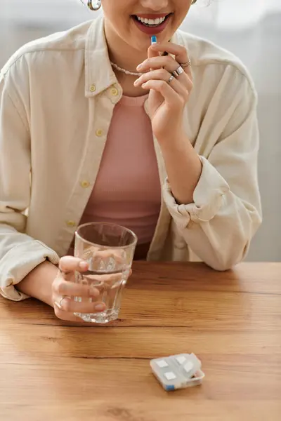 A young woman smiles as she prepares to take a pill with a glass of water beside her. — Stockfoto