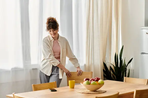 Smiling young woman arranges chairs at a cozy wooden table filled with fresh fruits and a drink. — Stock Photo