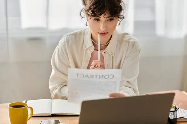 Une jeune femme examine soigneusement un contrat dans son espace de travail élégant, sirotant un café tranquillement. — Photo de stock