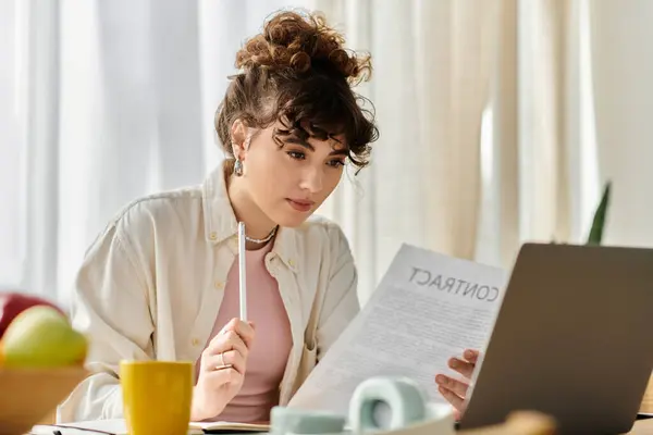 A young woman sits at a table, examining a document while holding a pen, in a well lit room. — Stock Photo