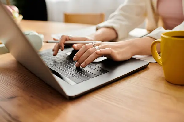A young woman types on her laptop, enjoying a warm drink in a sunny, cozy workspace. — Stock Photo