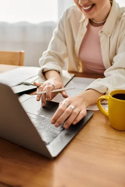 Una mujer alegre toma notas en su portátil, bebiendo café en un espacio acogedor. - foto de stock