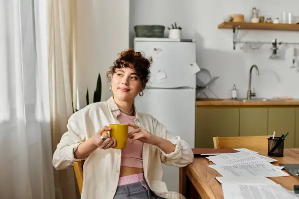 A young woman relaxes with a yellow mug in her cozy kitchen, surrounded by natural light. — Stock Photo
