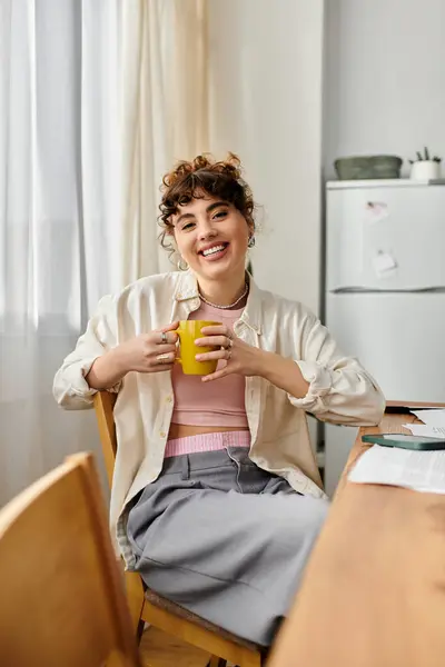 Relaxing at home, a young woman smiles while holding a bright yellow mug, exuding warmth. — Stock Photo