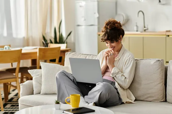A young woman is gleefully engaged with her laptop while relaxing in a sunlit living room. — Stock Photo