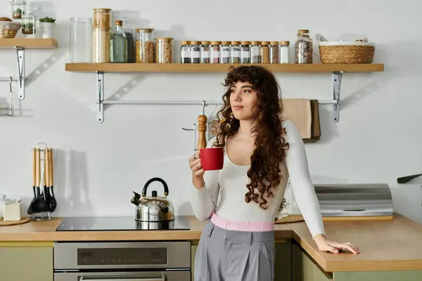 Une jeune femme sirote une boisson chaude dans sa cuisine élégante, entourée d'essentiels culinaires. — Photo de stock