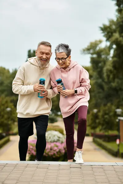 A mature couple enjoys a sunny day in the park, laughing and sipping drinks together. — Stock Photo