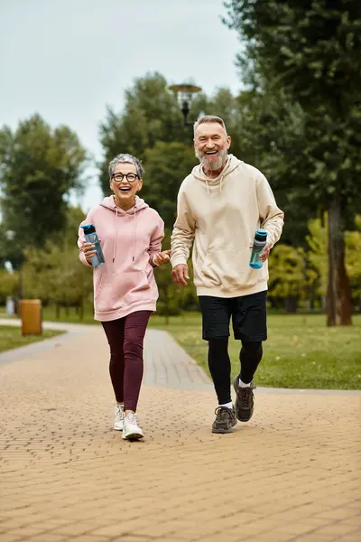 Two happy seniors jog together in a scenic park, sharing a moment filled with joy and connection. — Stock Photo