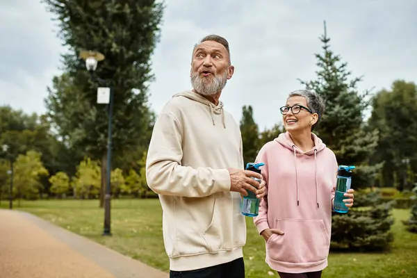 A loving mature couple strolls hand in hand through a vibrant park, sharing smiles and laughter. — Stock Photo