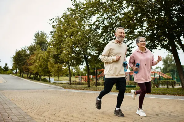 A mature couple jogs happily on a serene path, enjoying their morning together. — Stock Photo