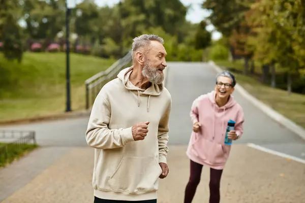 A joyful man and woman share laughter while jogging together in a beautiful park. — Stock Photo