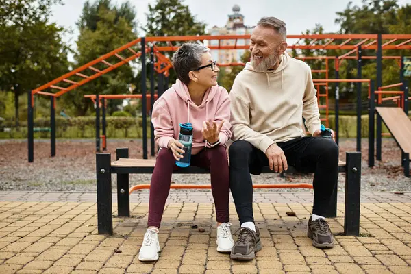 Um casal amoroso compartilha risos em um banco em uma área de fitness ao ar livre no parque. — Fotografia de Stock