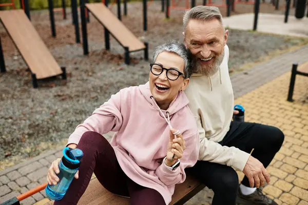 A mature couple happily sits on a bench, laughing and sharing joyful moments after exercising. — Stock Photo