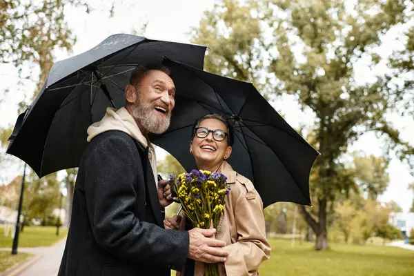 A mature couple braves the rain while smiling and enjoying each others company in a park. — Stock Photo