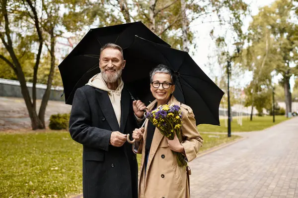 Ein liebevolles Seniorenpaar geht Hand in Hand und teilt Lächeln und Blumen in einer ruhigen Parklandschaft. — Stockfoto