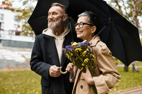 A loving couple enjoys each others company while walking in the park, holding flowers. — Stock Photo