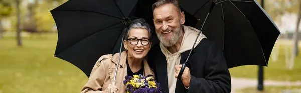 Loving couple enjoys a joyful moment together outdoors, holding an umbrella and flowers in fall. — Stock Photo
