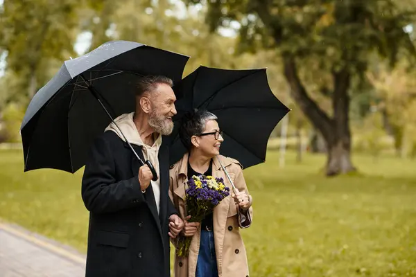 A loving couple walks in the park, sharing smiles and umbrellas in the rain. — Stock Photo