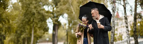 A mature couple strolls under an umbrella, sharing laughter and love in a serene park setting. — Stock Photo