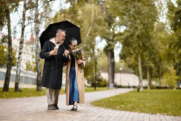 A charming couple enjoys a peaceful walk in a park, sharing smiles while holding an umbrella. — Stock Photo