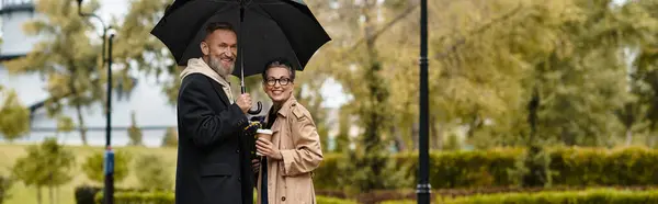 Mature couple enjoys each others company while staying dry under an umbrella in the park. — Stock Photo