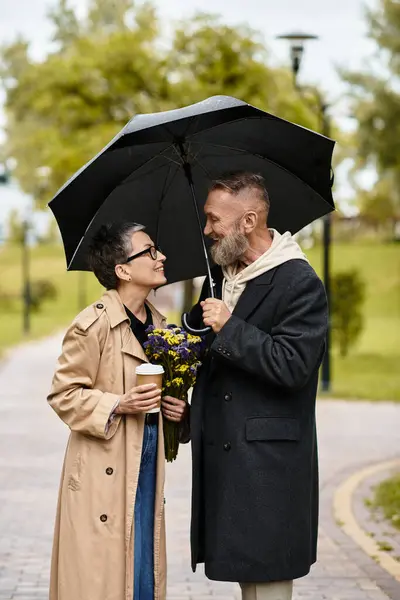 Joyful couple enjoys each others company with flowers and coffee while sheltering from the rain. — Stock Photo