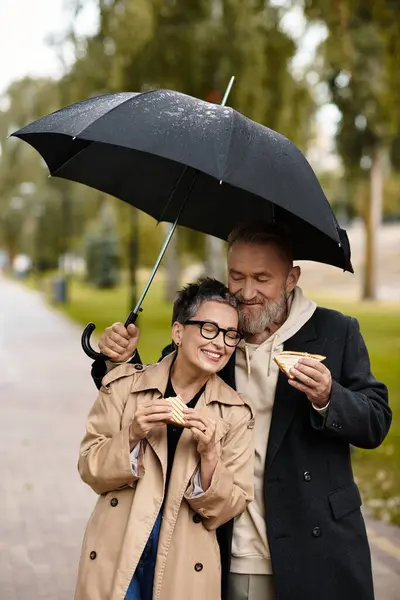 Una coppia matura condivide momenti dolci gustando spuntini insieme, al riparo dalla pioggia. — Foto stock