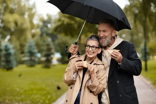 A mature couple cherishes a rainy day together, smiling and savoring delicious snacks. — Stock Photo