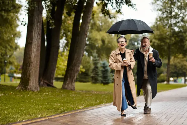 Couple laughs together under an umbrella while walking in the rainy park. — Stock Photo