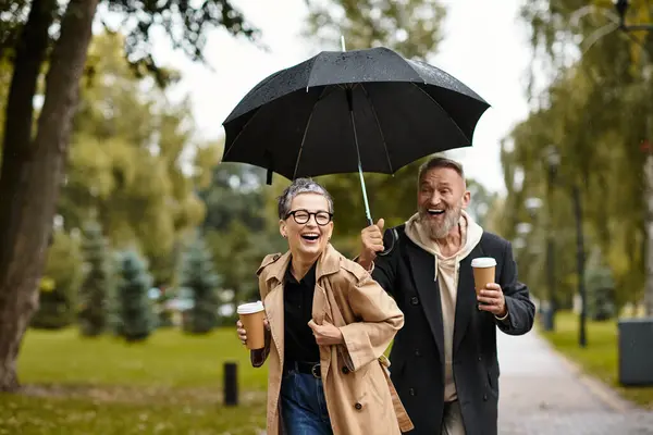 Ein reifes Paar genießt die Gesellschaft des anderen, während es sich spielerisch einen Regenschirm teilt. — Stockfoto