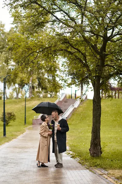 A mature couple shares a loving glance while sheltered by an umbrella on a rainy day. — Stock Photo