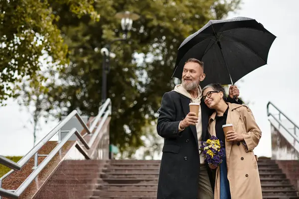 On a rainy day, a loving couple smiles while enjoying warm drinks, surrounded by nature and joy. — Stock Photo