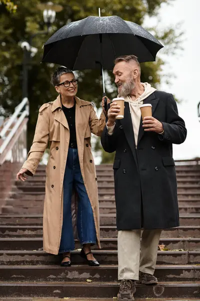 A loving couple strolls down stairs, sharing smiles while holding coffee cups in light rain. — Stock Photo