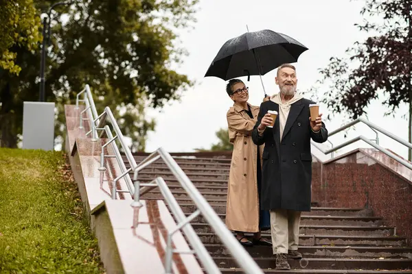 Mature couple enjoys each others company, laughing while walking down steps on a rainy day. — Stock Photo