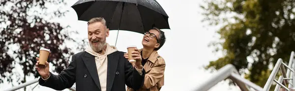A loving couple enjoys playful moments while strolling in a park with coffee during light rain. — Stock Photo