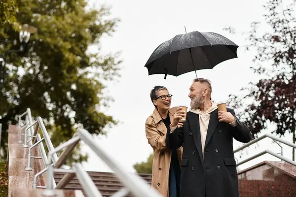 A mature couple enjoys warmth and laughter while walking down a staircase under an umbrella. — Fotografia de Stock