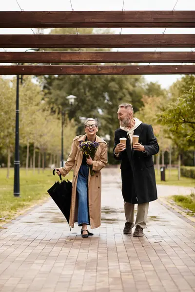 A mature couple walks hand in hand in a park, radiating love and joy while holding coffee. — Stock Photo