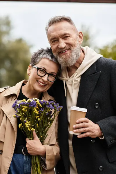 Una coppia amorevole condivide un caldo abbraccio mentre tiene fiori e caffè, irradiando gioia. — Foto stock