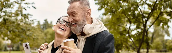 A delightful couple shares laughter while sipping coffee and capturing special memories outdoors. — Stock Photo
