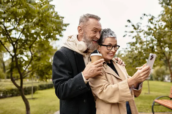 Um casal amoroso sorri enquanto usa um smartphone em um ambiente de parque sereno, compartilhando um momento alegre. — Fotografia de Stock