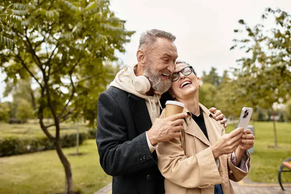 Pareja cariñosa comparte la risa y el calor mientras revisa sus teléfonos en un parque escénico. - foto de stock