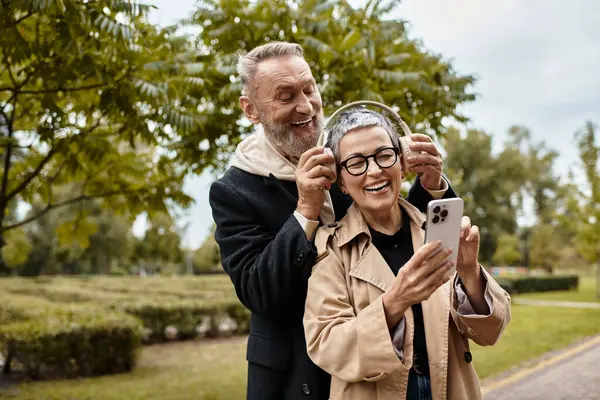 Pareja madura disfrutando de la música juntos mientras exploran un hermoso parque en otoño. - foto de stock