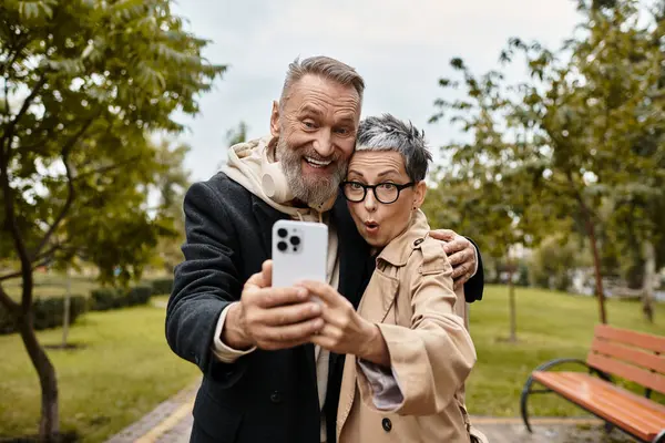 Una pareja madura sonriendo y posando juntos mientras se toma una selfie en un hermoso parque. - foto de stock