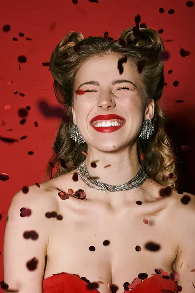 A stylish woman laughs joyfully among falling rose petals on a vibrant red backdrop. — Stock Photo